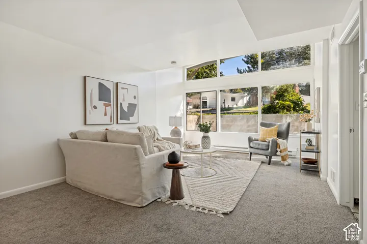 Spacious room featuring vaulted ceilings, expansive windows, light-toned walls, and grey carpeting