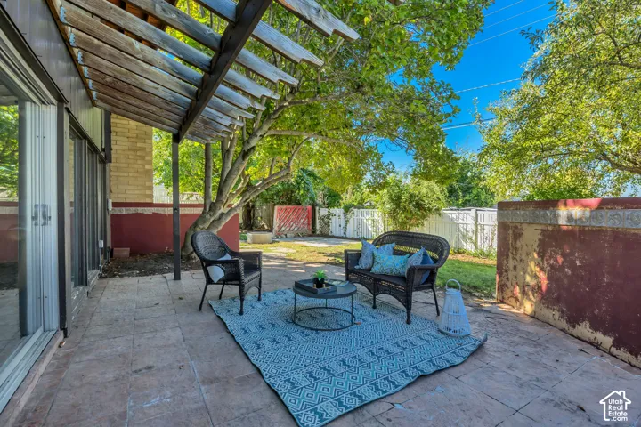 Expansive stamped concrete patio with a wooden pergola, mature trees, and privacy fencing