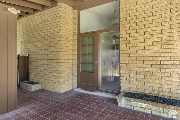 Brick exterior featuring a wood-frame door with glass panels, an expansive fixed glass panel, and a tiled patio