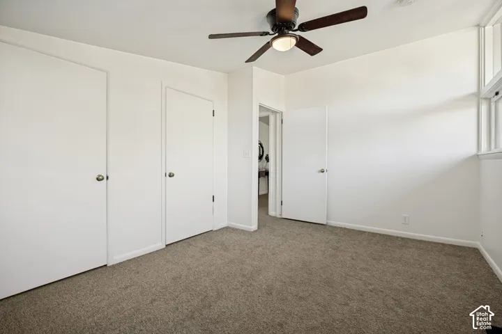Neutral tone wall paint, textured carpet flooring, two paneled doors with spherical hardware, a ceiling fan with integrated lighting, and high-set horizontal windows