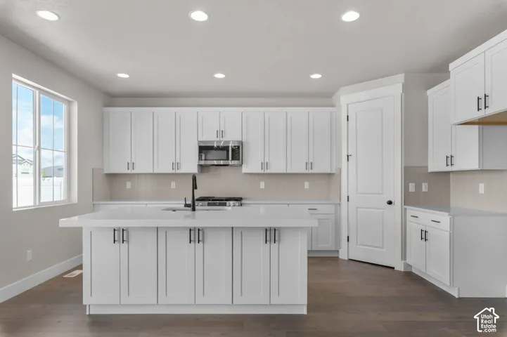 Kitchen featuring a central island, white cabinetry, integrated stainless steel microwave, black hardware, and wood-finish flooring