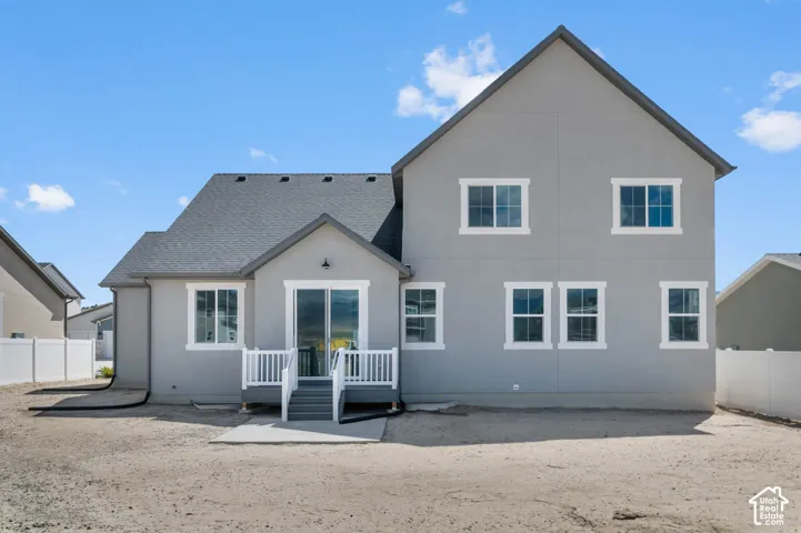 Rear exterior with gray stucco finish, multiple windows with white trim, a sliding glass door, a built-in deck with railings, and a dark shingle roof