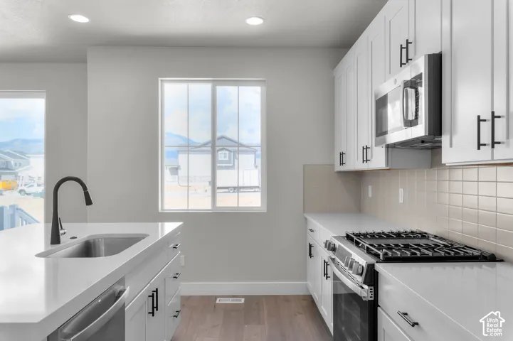Modern kitchen featuring white cabinetry, stainless steel appliances, a gas range, and a matte black gooseneck faucet