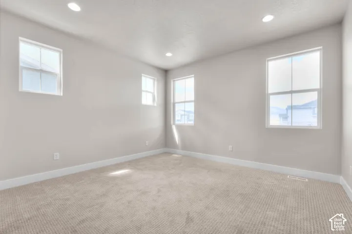Recessed lighting illuminating the neutral-toned walls, multiple windows, and light-colored carpeting