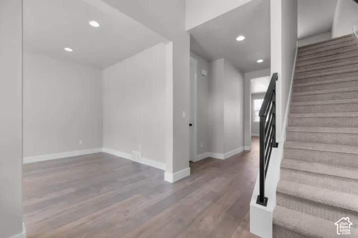 Recessed lighting, wood-finish flooring, staircase with carpeting, black metal balusters, and white trim throughout