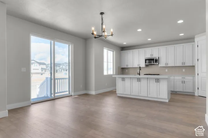 Spacious kitchen featuring white cabinetry, an island with integrated sink, stainless steel microwave, and recessed lighting