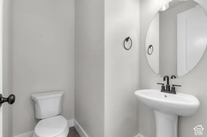 Pedestal sink with matte black faucet, round wall mirror, and modern toilet