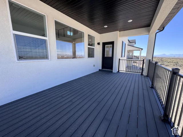 Covered deck with dark wood-finish decking, black metal railing, recessed lighting, and a black exterior door
