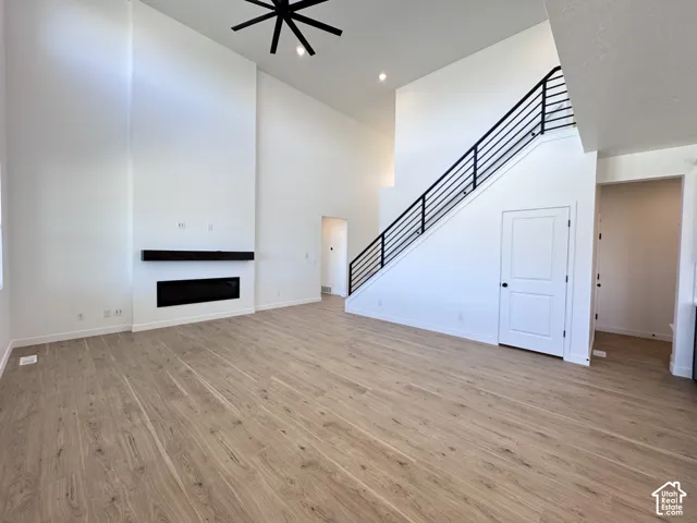 Spacious room featuring high ceilings, wood-finish flooring, a built-in electric fireplace with a dark mantel, and a staircase with a black metal railing