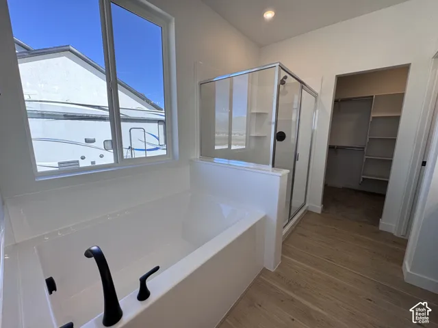 White soaking tub with matte black fixtures, glass-enclosed shower, wood-finish flooring, and a built-in closet system