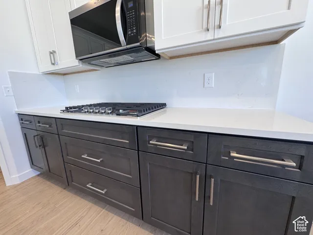 White upper cabinetry with brushed nickel hardware, stainless steel microwave, gas cooktop, light-toned countertops, and wood-finish flooring