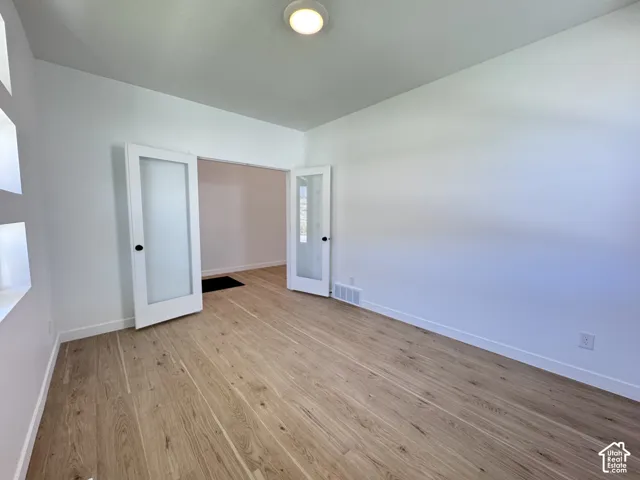 Wood-finish flooring throughout, white walls, double doors with frosted glass panels, and a flush-mount ceiling light