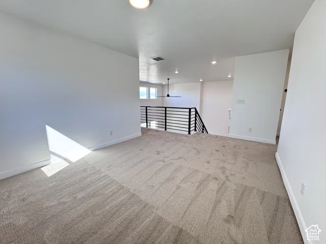 Spacious carpeted area featuring recessed lighting, a modern ceiling fan, and a black horizontal bar railing