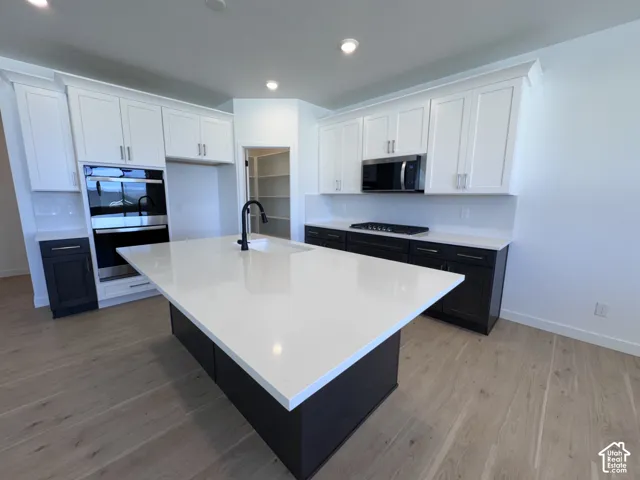 Kitchen featuring white upper cabinetry, dark lower cabinetry, and a large central island with a white countertop