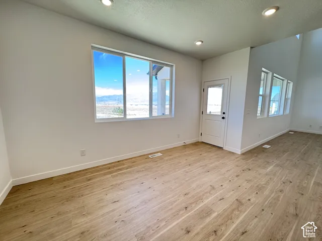 Recessed lighting, white walls, wood-finish flooring, multiple windows, and a panel door with a clear glass insert