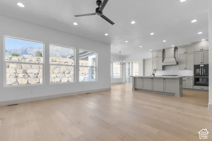 Spacious open-concept interior featuring light wood-finish flooring, recessed lighting, and a kitchen with light gray cabinetry, a large island, and built-in double ovens