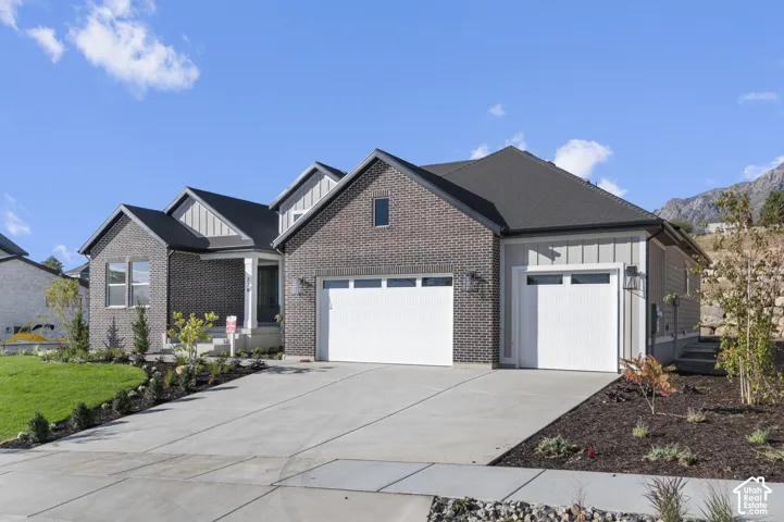 Contemporary exterior featuring brick and board-and-batten siding, a dark shingle roof, a concrete driveway, and integrated garage doors