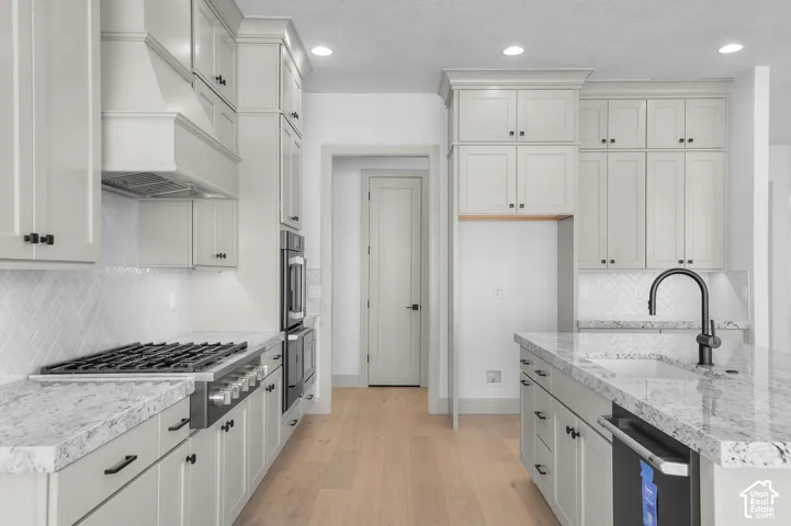 Expansive kitchen featuring light-toned cabinetry, a large kitchen island with a built-in sink and faucet, integrated wall ovens, and a gas range