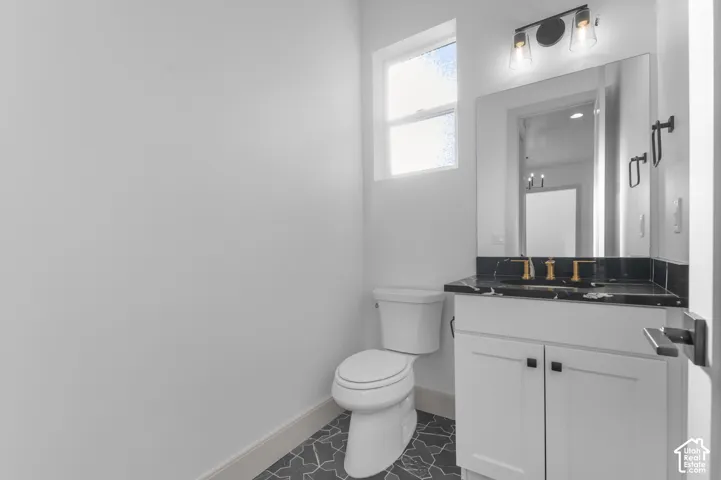 White vanity with a dark stone countertop and gold-finish fixtures