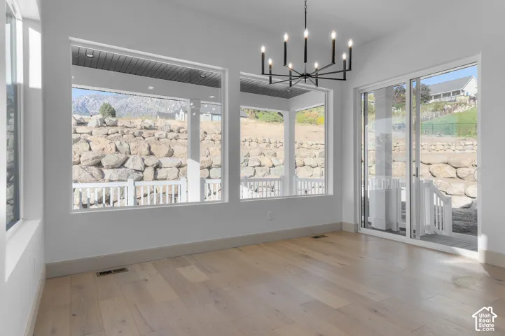 Hardwood-style flooring, contemporary chandelier, sliding glass door, multiple large windows, and white walls