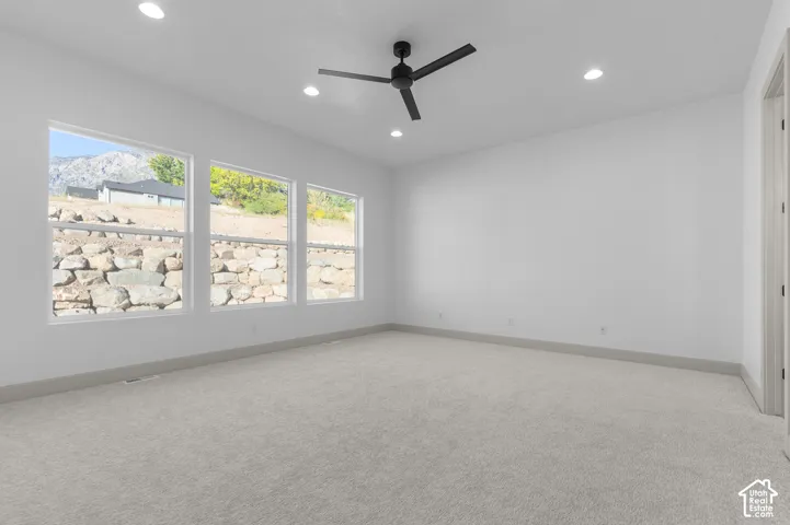 Recessed lighting, light gray carpeting, matte black ceiling fan, white interior walls, and three large windows