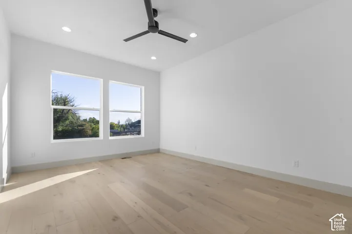 Light wood-finish flooring, recessed ceiling lighting, dual windows, modern ceiling fan, and white wall finishes