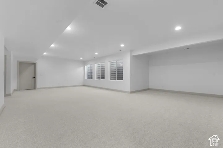 Expansive room featuring recessed lighting, a neutral carpet, three egress windows with blinds, and white walls