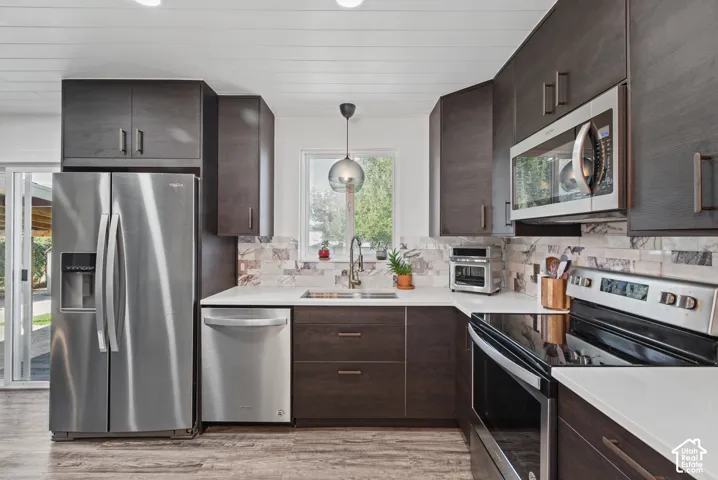 Contemporary kitchen featuring dark wood-finish cabinetry, stainless steel appliances, white countertops, and a patterned backsplash