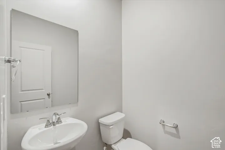 Pedestal sink with chrome faucet, wall-mounted mirror, and white toilet