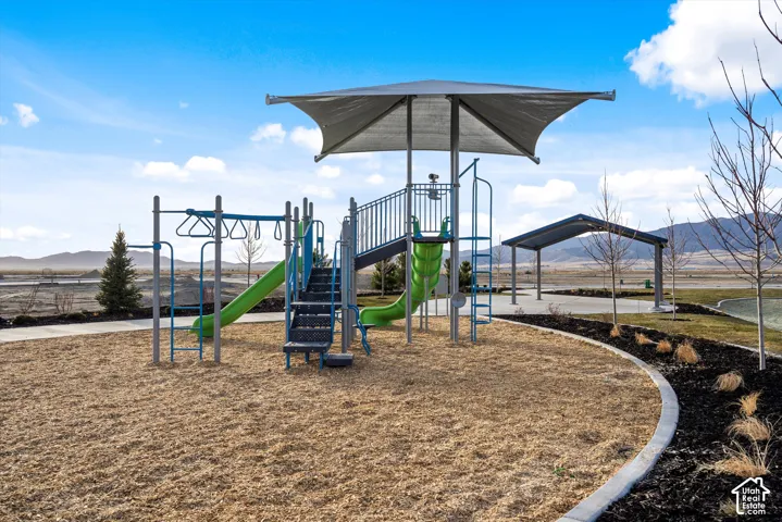 Playground with a shade structure, two slides, climbing elements, and a paved walkway