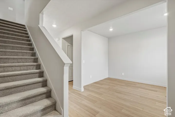 Carpeted staircase with white railings, recessed lighting, and wood-finish flooring