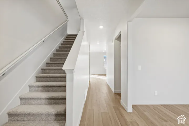 Carpeted staircase with white handrail, wood-finish flooring, and recessed lighting