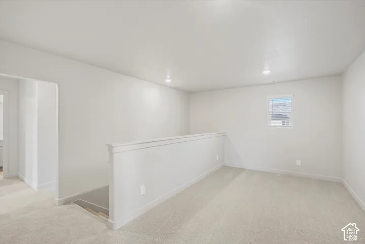 Carpeted upstairs area featuring a window, recessed lighting, and a partial wall with a railing