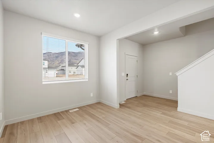 Recessed lighting, light wood-finish flooring, white trim, a large window, and a crisp white door