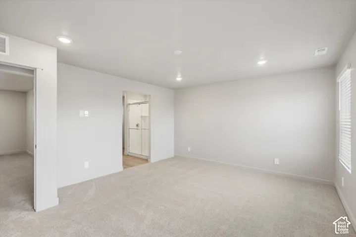 Expansive carpeted area with recessed lighting, an interior window, and access to an adjacent room with a glass-enclosed shower