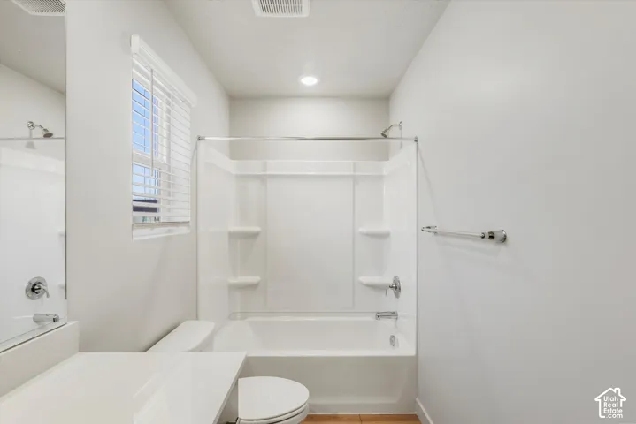 Full bathtub and shower combination with a bright window, recessed lighting, and a chrome towel bar