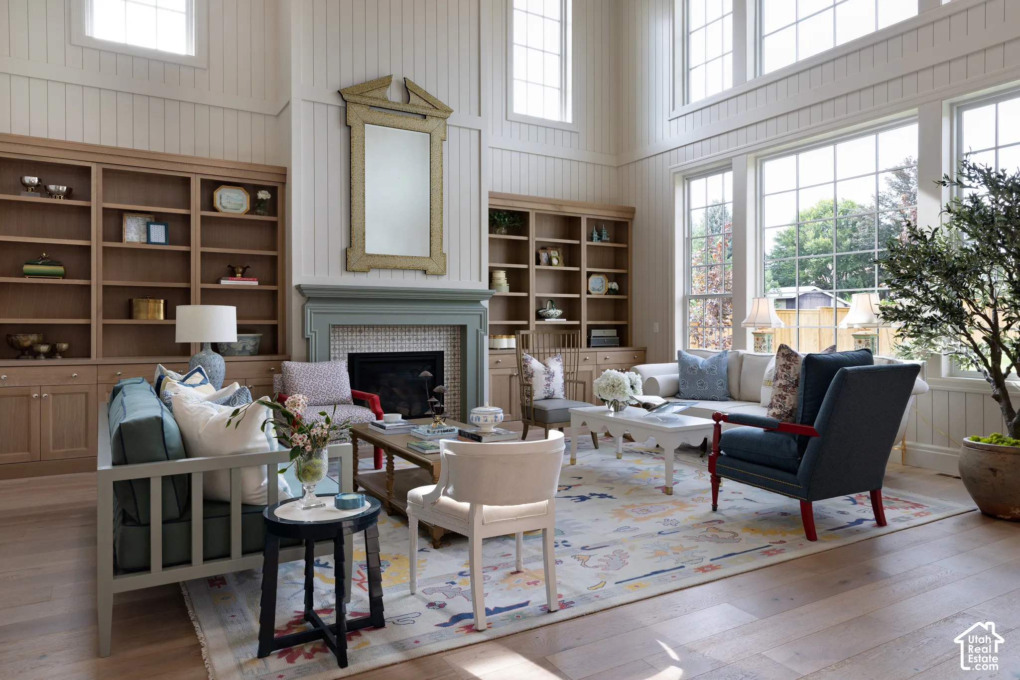 Vaulted ceiling featuring shiplap-paneled walls, built-in natural wood shelving, a fireplace with a tiled surround, and large multi-pane windows