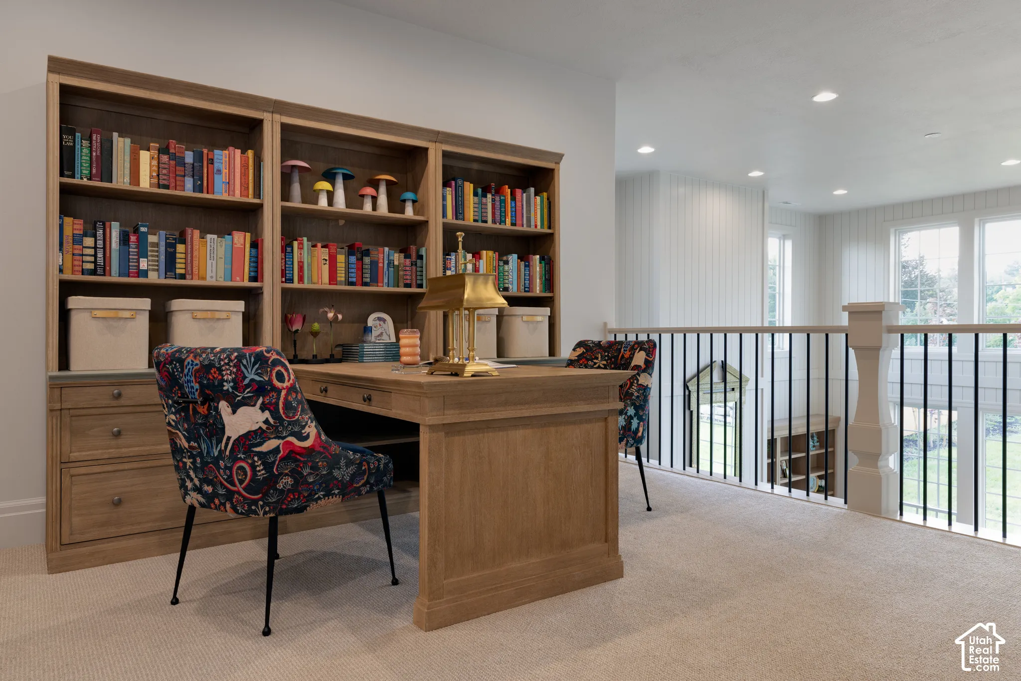 Built-in wood-finish shelving, wood-finish desk, light-colored carpeting, white spindle railing, and multiple windows providing natural light