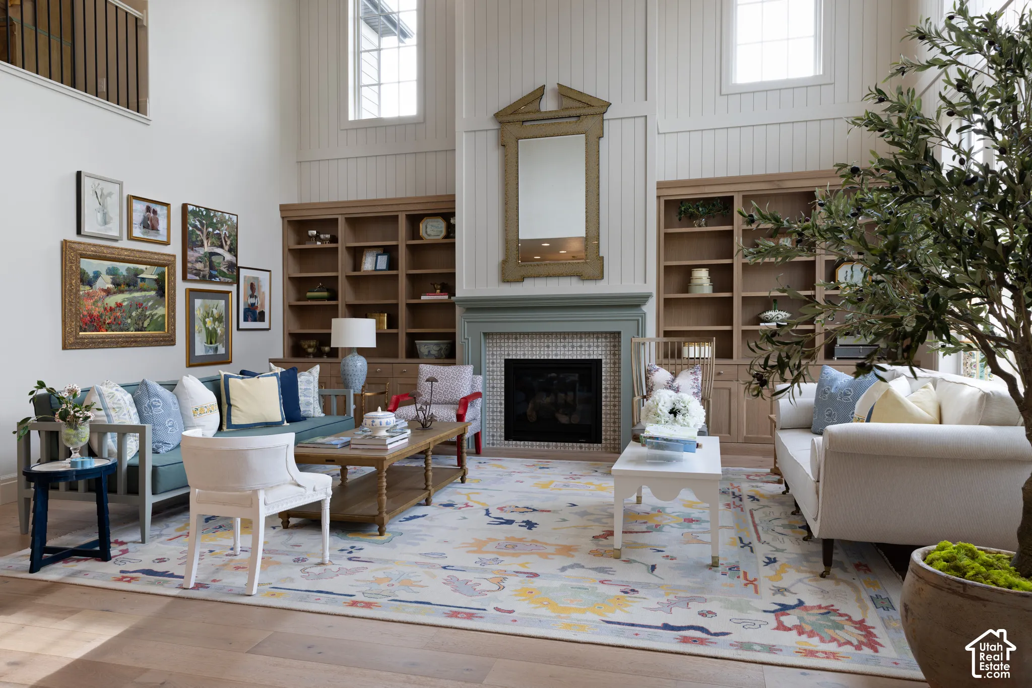Vaulted ceiling with upper windows, integrated built-in shelving, wood-finish flooring, fireplace with tile surround, and an open-concept layout