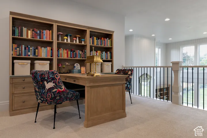 Built-in wood-finish shelving, wood-finish desk, light-colored carpeting, white spindle railing, and multiple windows providing natural light