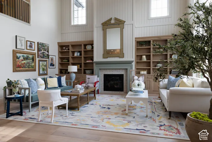 Vaulted ceiling with upper windows, integrated built-in shelving, wood-finish flooring, fireplace with tile surround, and an open-concept layout