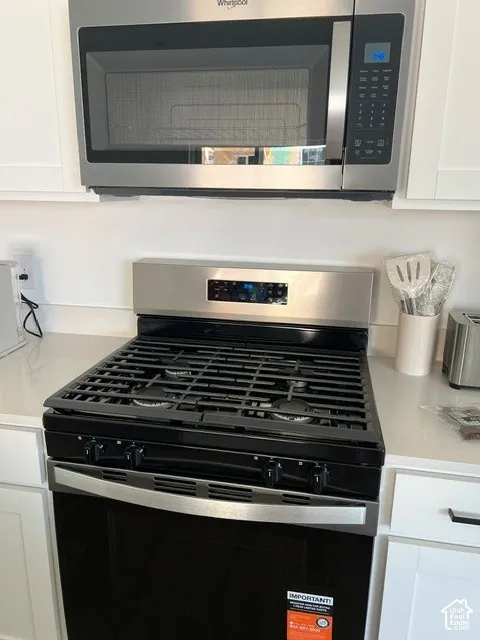 Stainless steel microwave, stainless steel range with black cooktop, white perimeter cabinetry, and white countertops