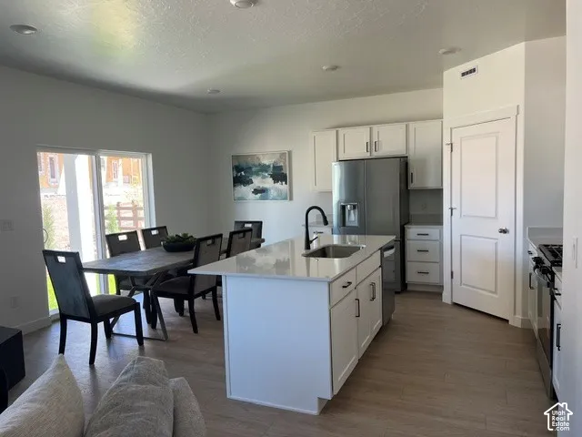 Kitchen and dining area featuring a center island with sink, stainless steel appliances, wood-finish flooring, white cabinetry, and sliding glass doors