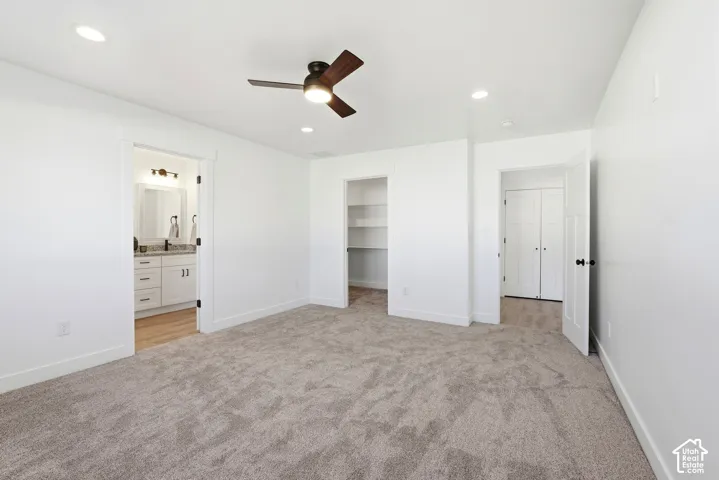 PRIMARY BEDROOM- Recessed lighting, ceiling fan, carpet flooring, a walk-in closet with built-in shelving, and an en-suite bathroom with a vanity and wood-finish flooring