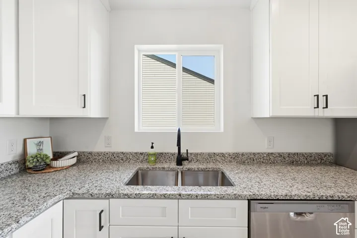 White shaker cabinetry, speckled countertops, dual-basin stainless steel sink, black matte faucet, and a stainless steel dishwasher
