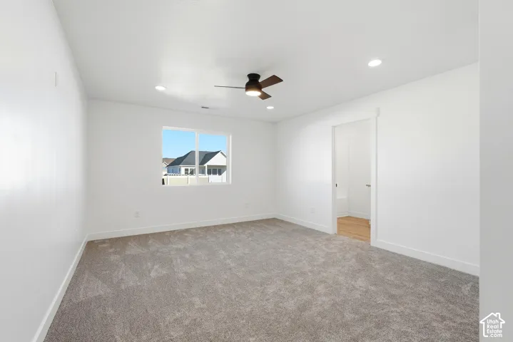 Spacious room with plush gray carpeting, recessed lighting, a modern ceiling fan, and a light wood-finish flooring visible through the doorway