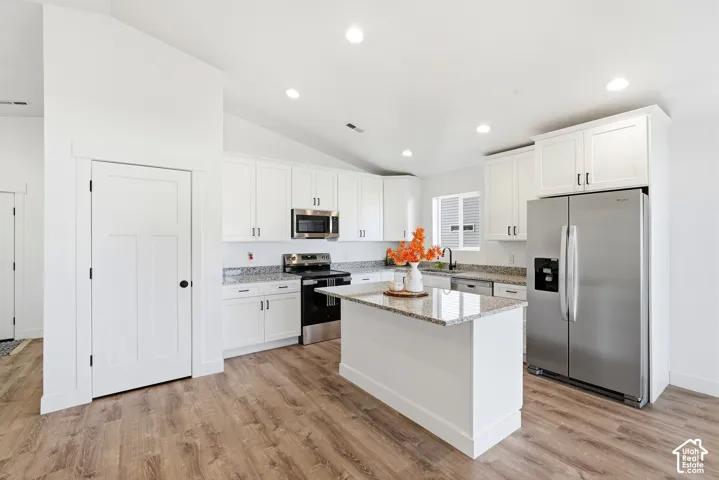 Kitchen featuring white cabinetry, granite countertops, stainless steel appliances, a center island, and wood-finish flooring