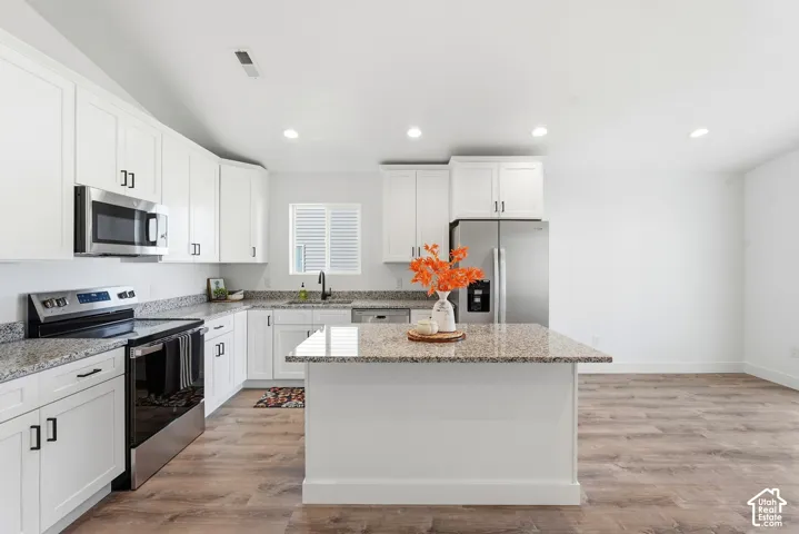 Kitchen featuring white cabinetry, granite countertops, stainless steel appliances, a kitchen island, and wood-finish flooring