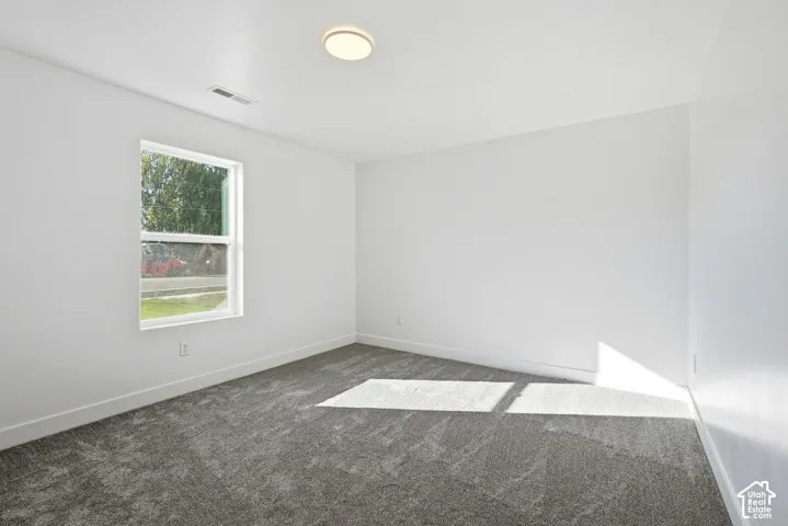 Neutral white walls with a single window, overhead flush-mount lighting, and gray patterned carpeting