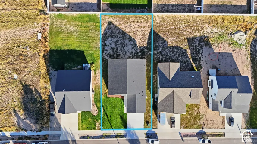 Aerial perspective showcasing a residential property with a dark shingle roof, a concrete driveway, and a partially manicured lawn